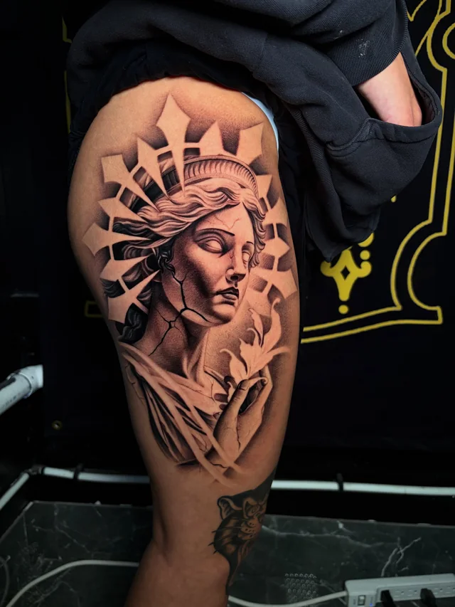 Black and grey crowned female figure with angular surrounding forms on a thigh.