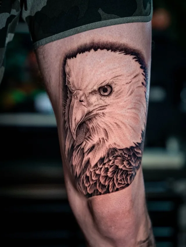 Detailed eagle head in profile in a black and grey tattoo on an upper arm.