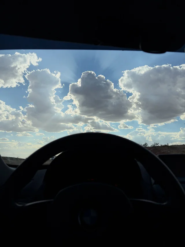 Road and bright clouds seen from inside a vehicle.