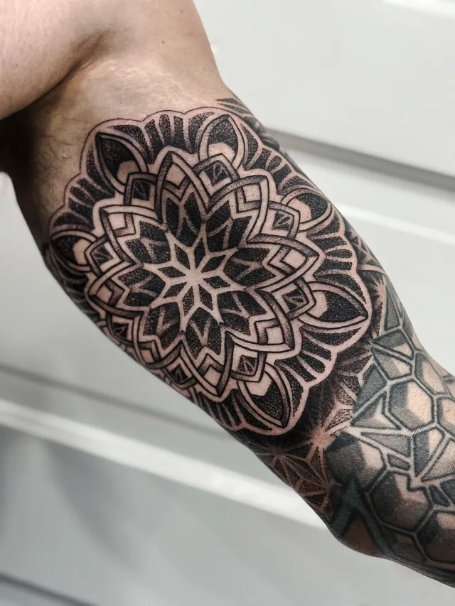Angled arm view of a layered mandala around the elbow, meeting adjoining geometric patterns.