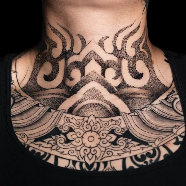 Front-neck tattoo with mirrored dark curls, rising tapered shapes and a pointed center above neighboring chest ornament.