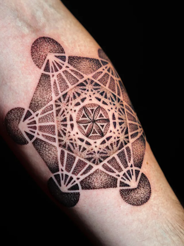 Close view of a geometric forearm tattoo with dark circular points, connecting lines and a six-petal center.