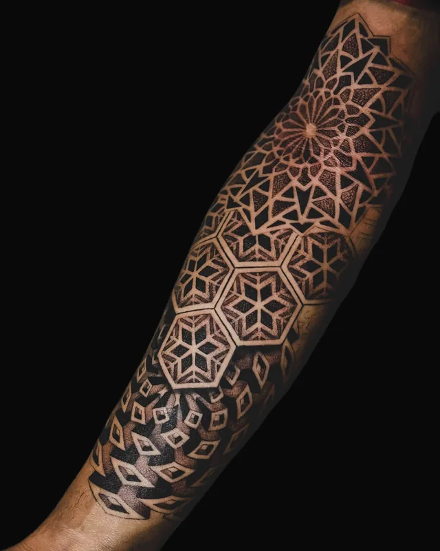 Forearm tattoo joining a large radial rosette, hexagonal flower panels and interlocking cube shapes.