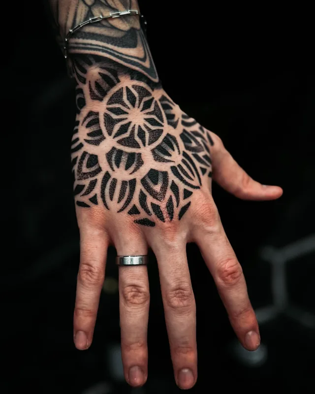 Black petal mandala tattoo across the back of a hand, connecting to curved wrist ornament.