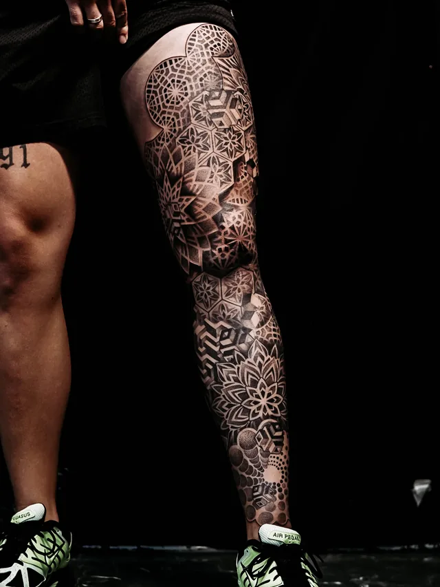 Leg tattoo extending from thigh toward the ankle with layered mandalas, hexagonal panels and repeating geometric grids.