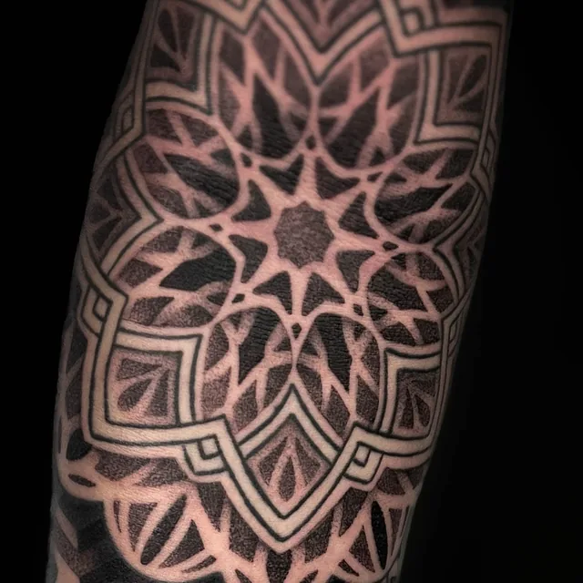 Close view of a star-centered mandala with layered petals and stepped borders on the forearm.