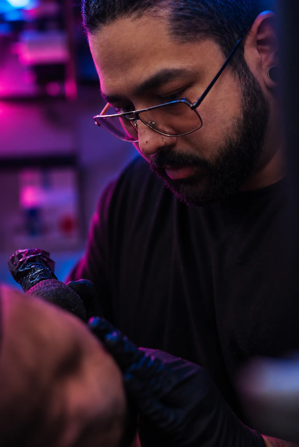 William Martz working with a tattoo machine, wearing glasses and black gloves.