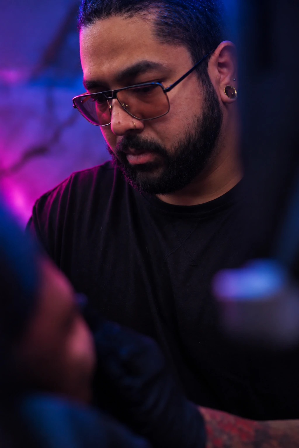 William Martz wearing glasses, focused on his work in blue and violet light.