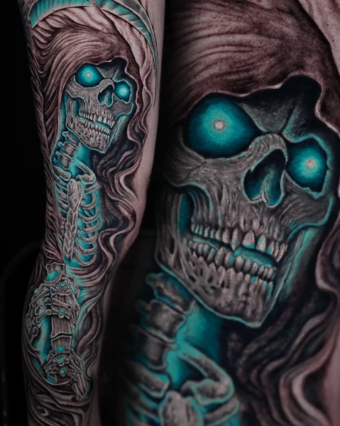 A hooded skull tattoo with bright turquoise eyes and flowing folds of fabric.