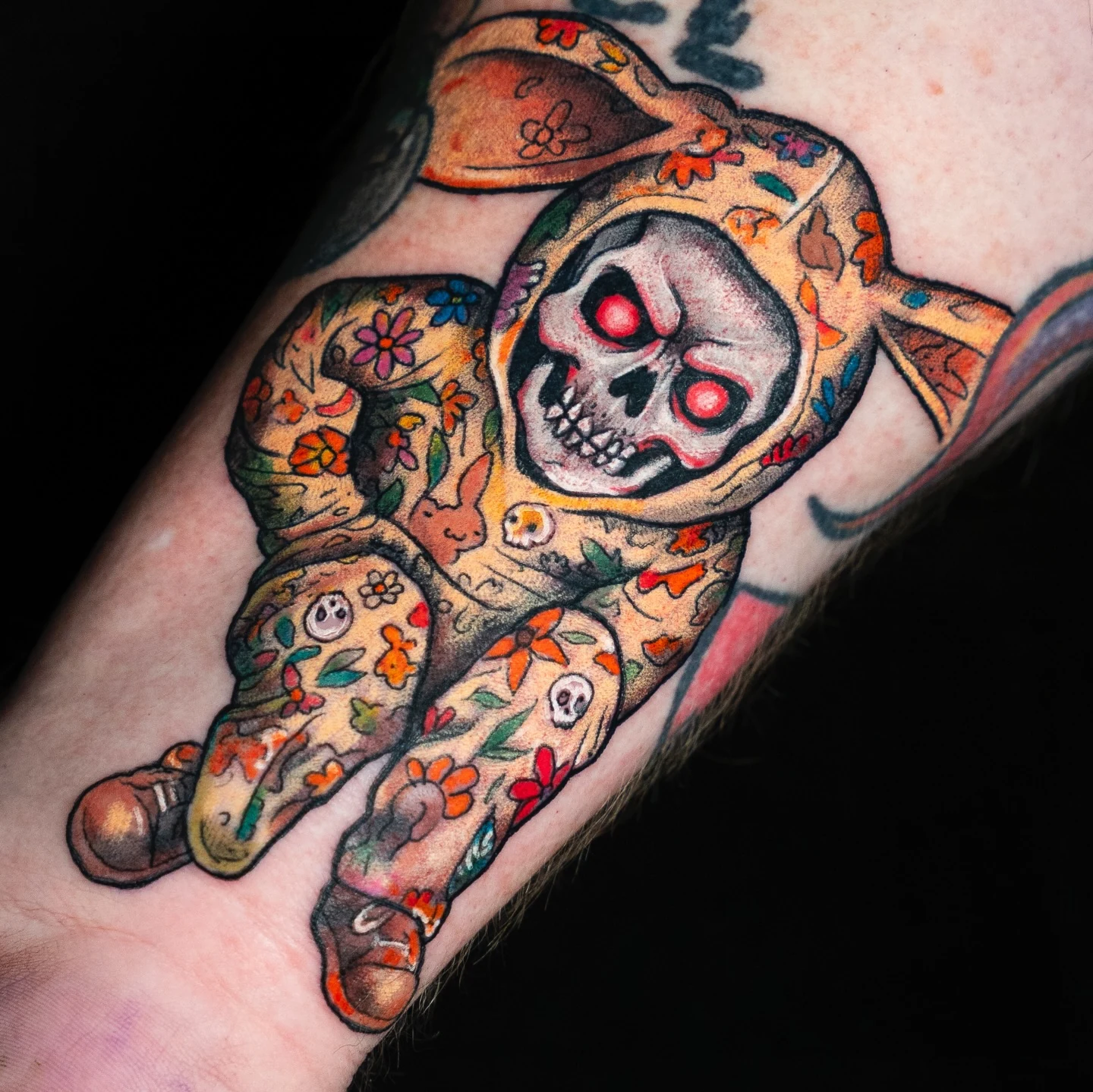 A colorful matryoshka-inspired tattoo with a skull face, glowing red eyes, and floral decoration.
