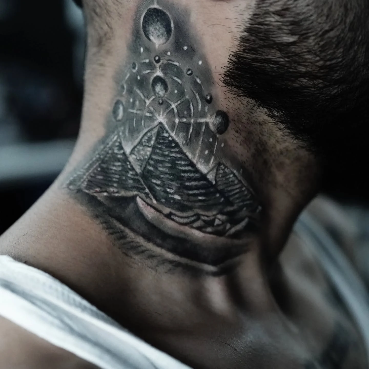 A black-and-gray neck tattoo combining pyramids, intersecting geometric lines, and moonlike circles.