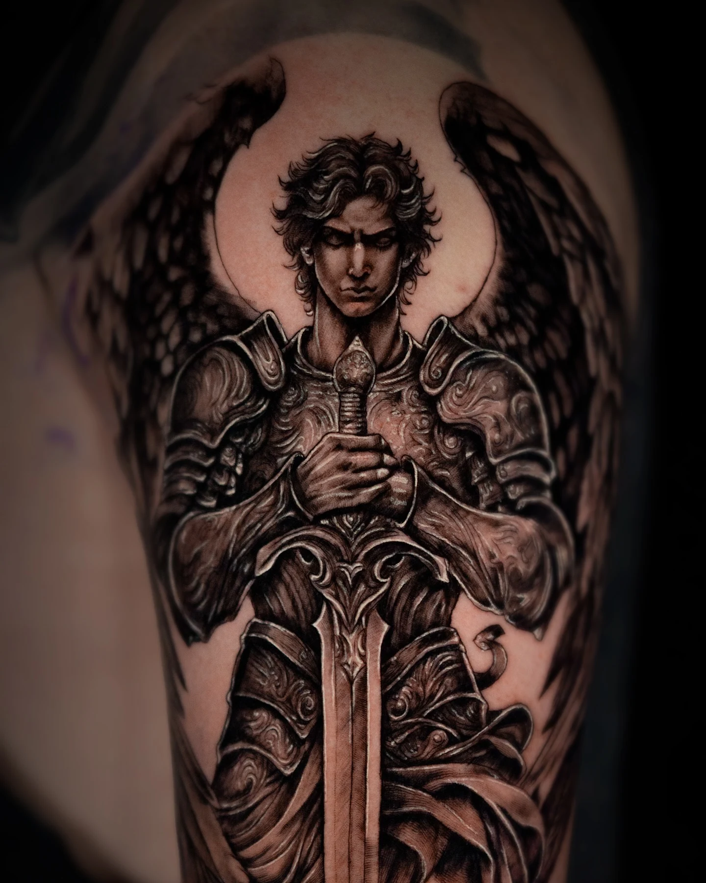 A black-and-gray winged guardian tattoo with armor and a long sword at the center.