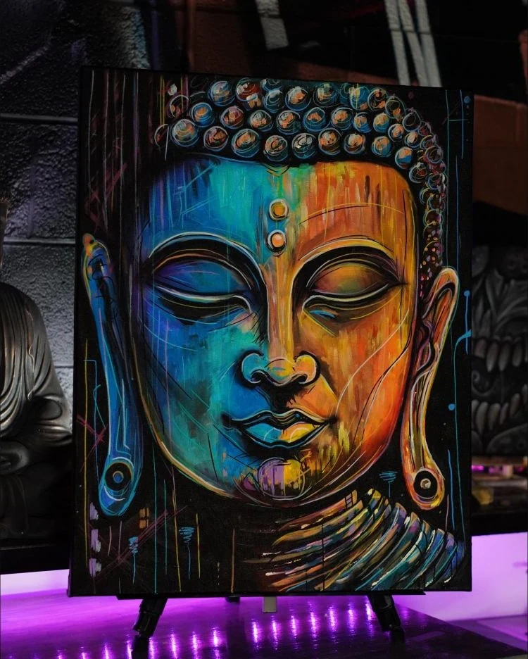 A painted Buddha portrait with turquoise shadows and bright orange and yellow light across the face.