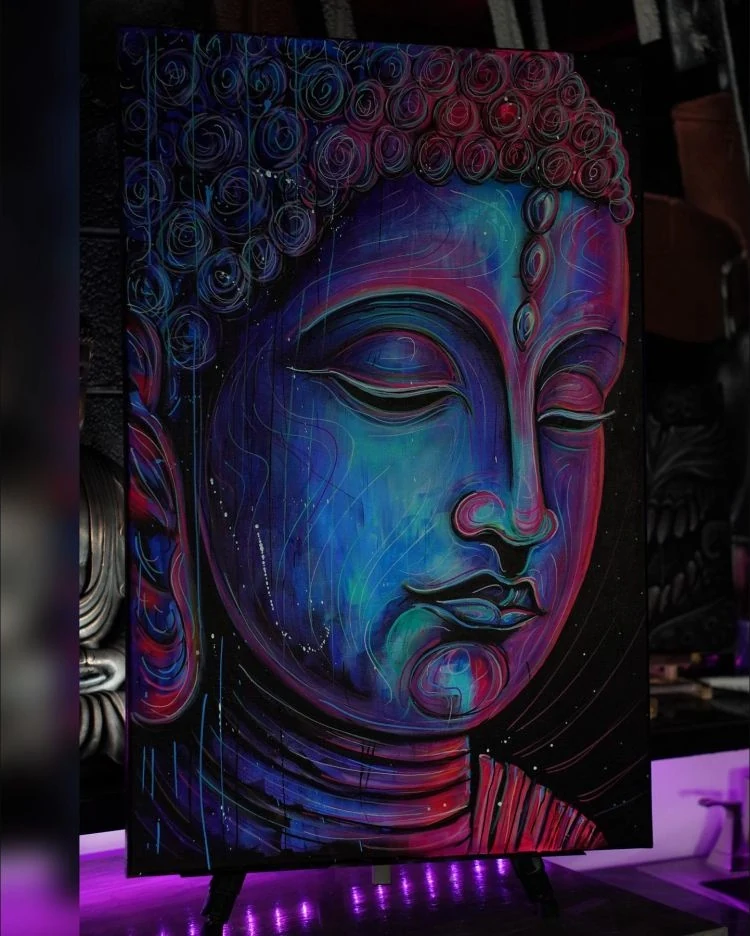 A painted Buddha portrait in blue, violet, and pink, with ornamental curls around the head.