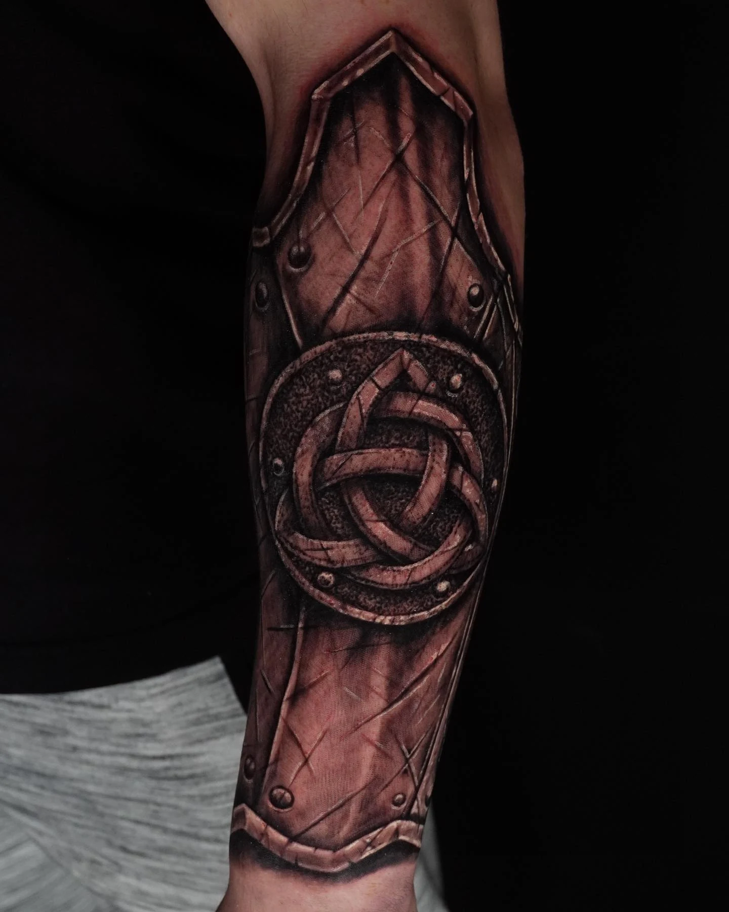 A black-and-gray forearm tattoo with a volleyball at the center of a textured, panel-like design.