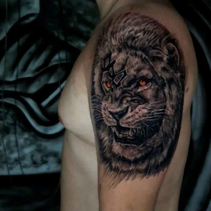 A roaring lion tattoo in black and gray with a warm accent in the eyes.