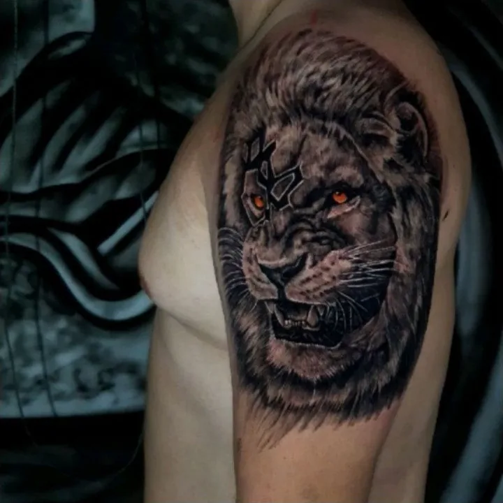 A roaring lion tattoo in black and gray with a warm accent in the eyes.