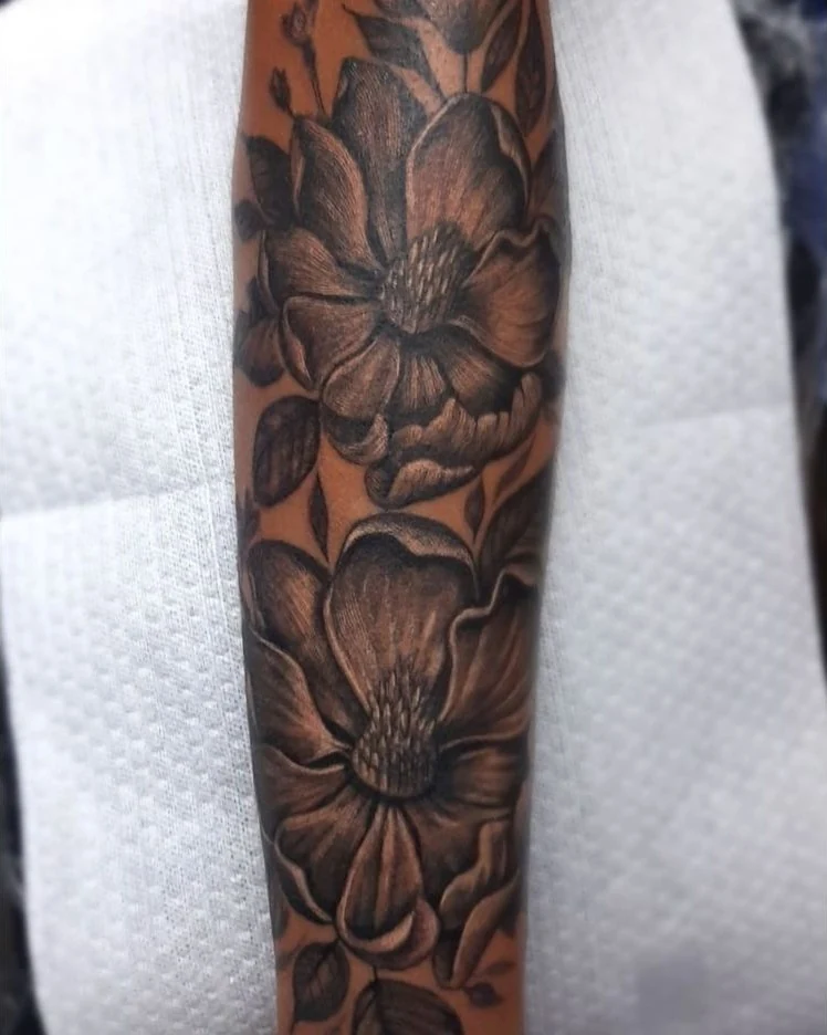 A black-and-gray floral tattoo with large overlapping blooms and shaded leaves.
