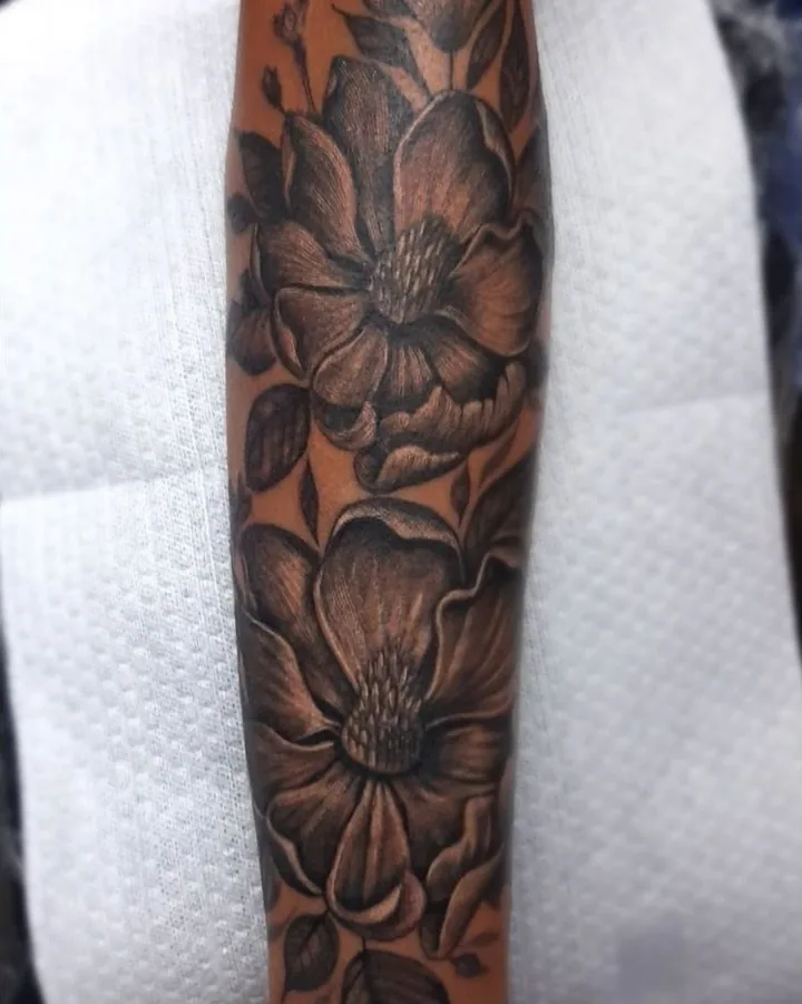 A black-and-gray floral tattoo with large overlapping blooms and shaded leaves.