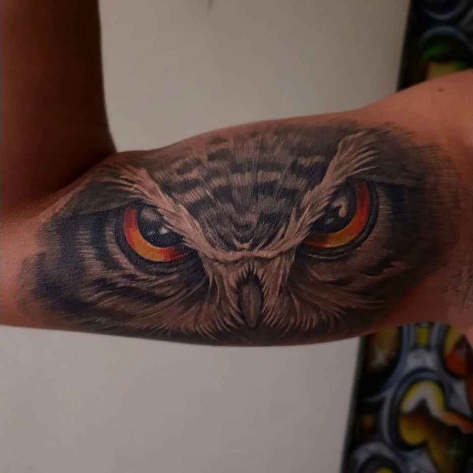A close-up owl gaze tattoo with orange eyes and finely shaded feathers.