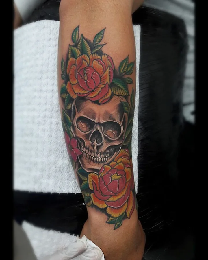 A colorful skull tattoo framed by red roses and green leaves.