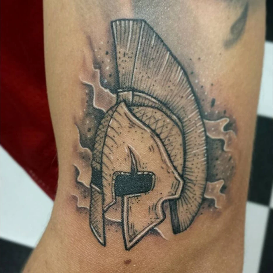 A black-and-gray Spartan-style helmet tattoo in profile.