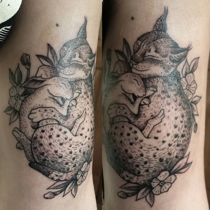 A curled sleeping fox tattoo surrounded by leaves and small flowers.