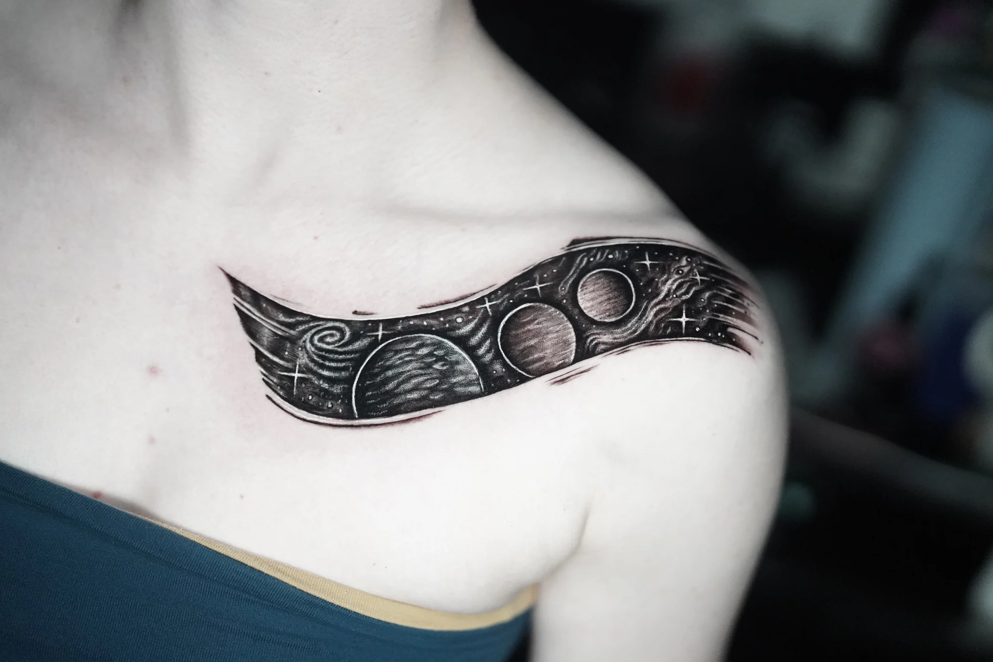 A curved black-and-gray ornamental tattoo following the collarbone.