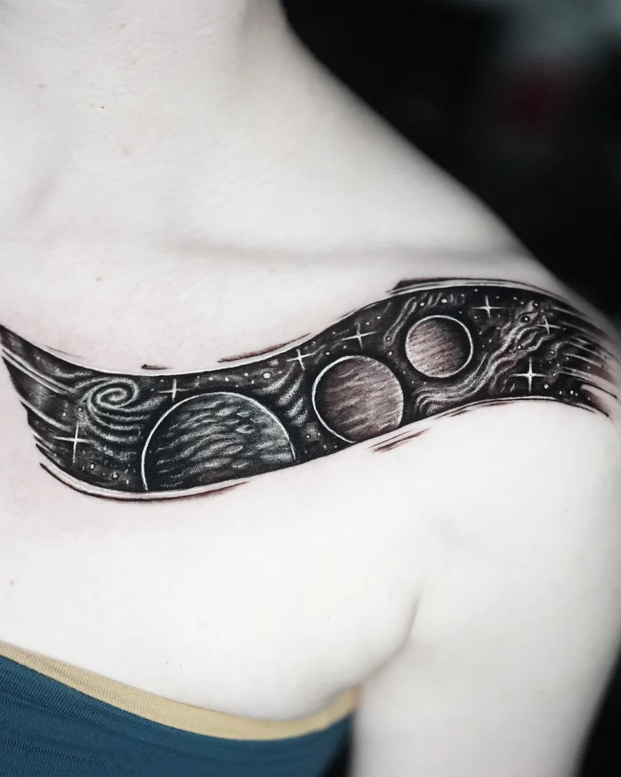 A curved black-and-gray ornamental tattoo following the collarbone.