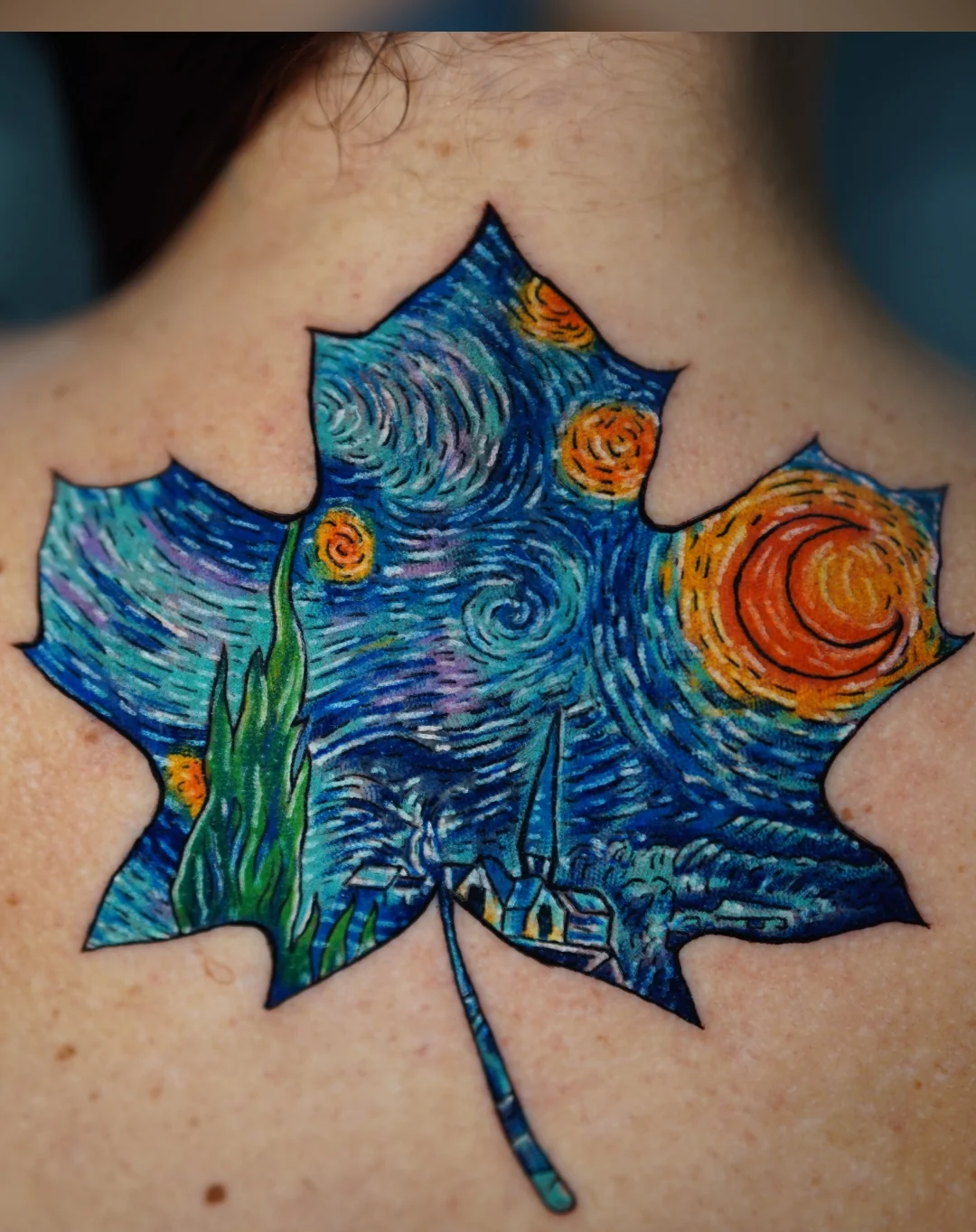 A maple leaf tattoo filled with a swirling night sky, blue brushlike marks, and golden stars.