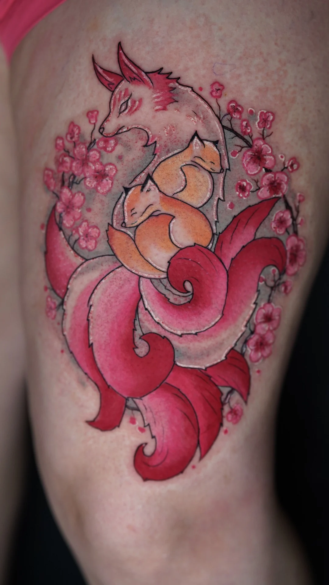 An orange fox tattoo surrounded by red flowing shapes and small blossoms.