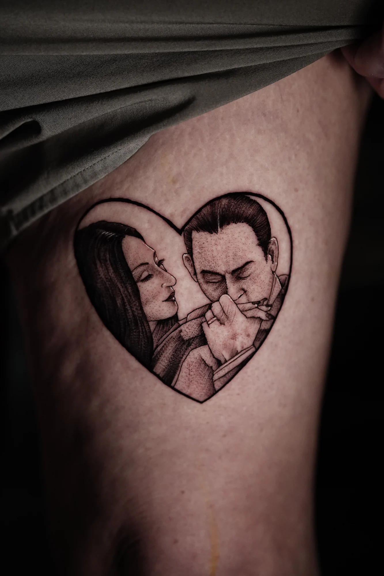 Gomez and Morticia Addams appear together inside a heart-shaped black-and-gray tattoo.