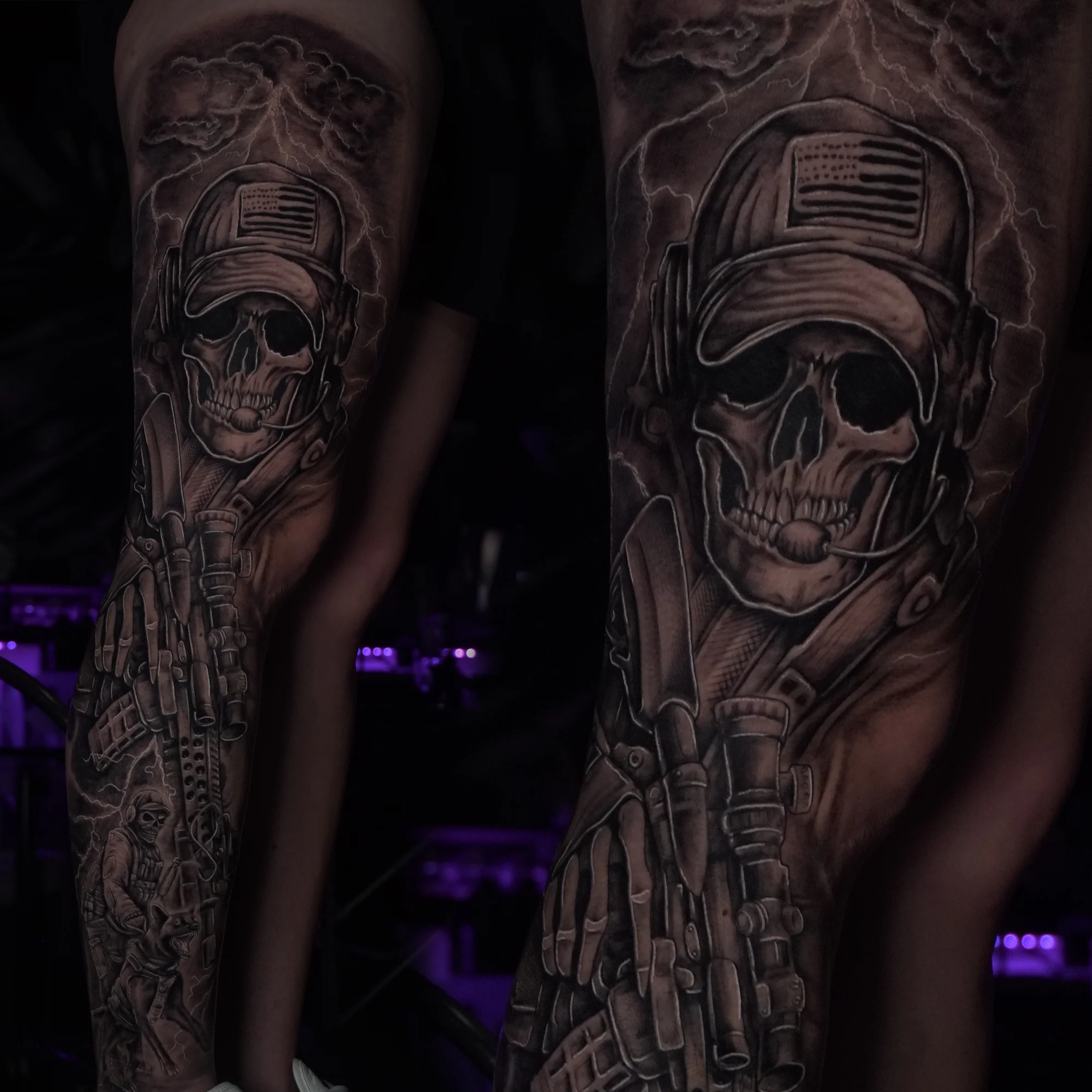 Two views of a black-and-grey leg tattoo depicting a skull-faced special operations soldier wearing a cap and communications headset, with a rifle and lightning.