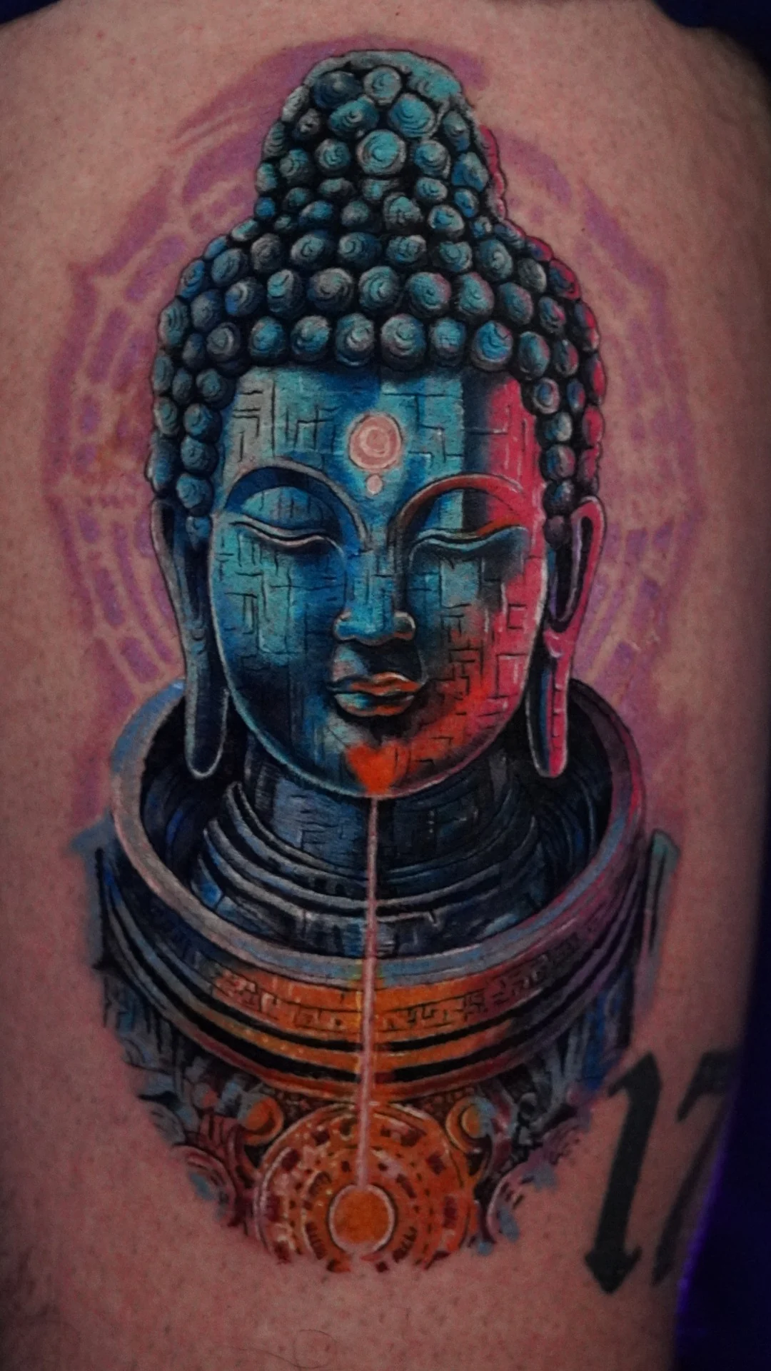 A colorful Buddha portrait tattoo built around turquoise, violet, and warm red highlights.