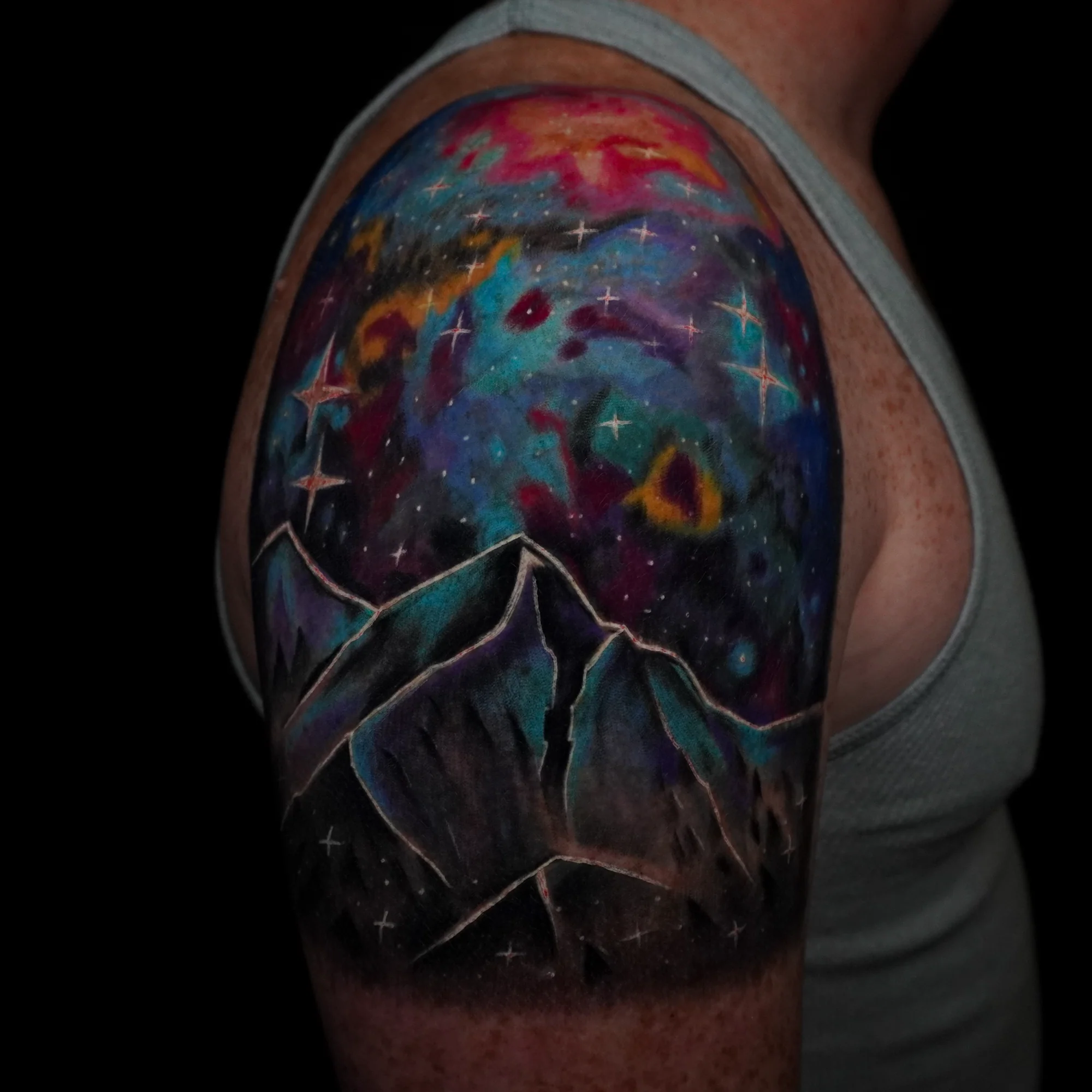 A colorful upper-arm landscape with dark mountain peaks beneath a luminous cosmic sky.