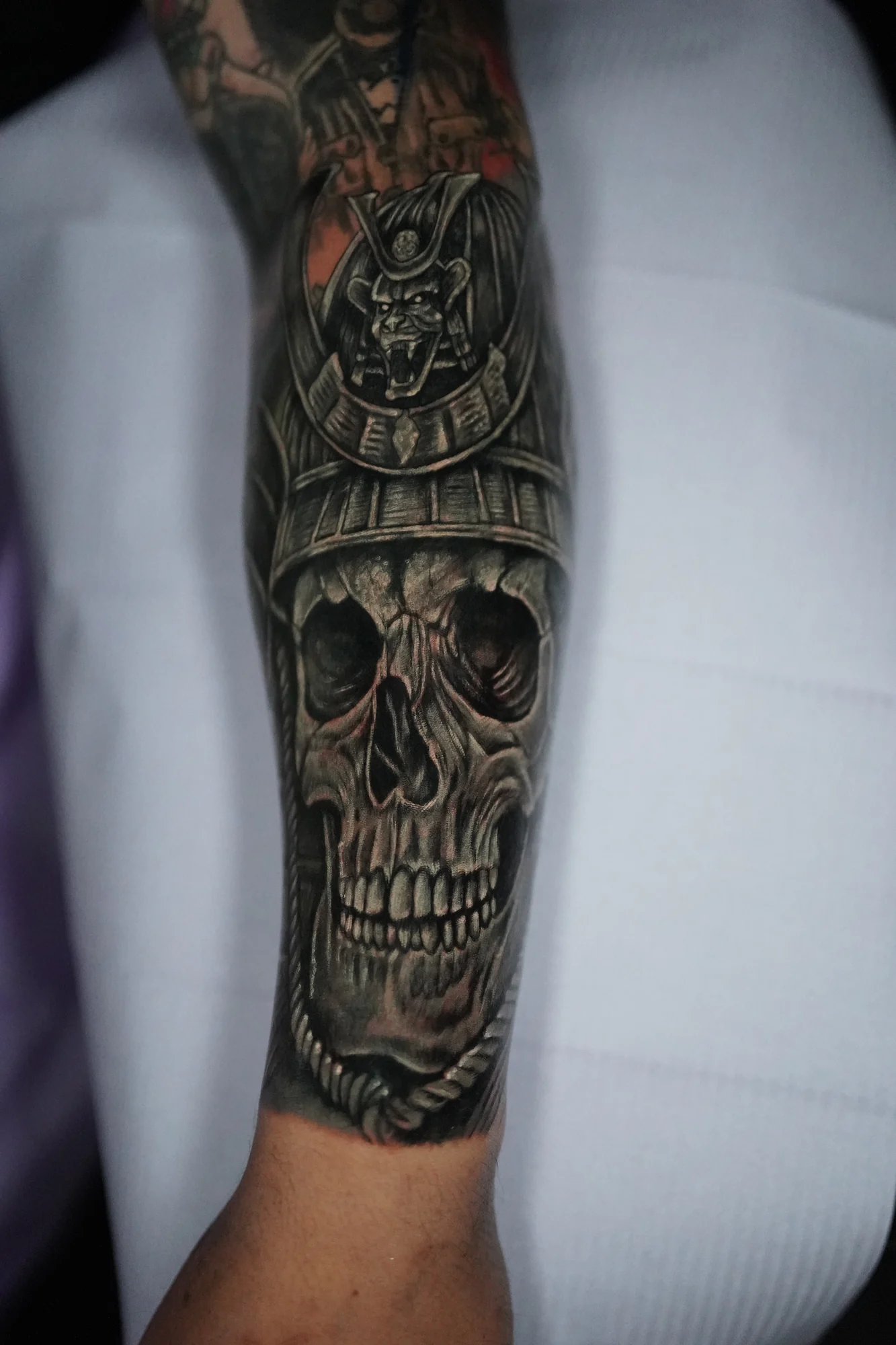 A realistic skull in a samurai helmet tattooed along the forearm, with a round crest above the brow.