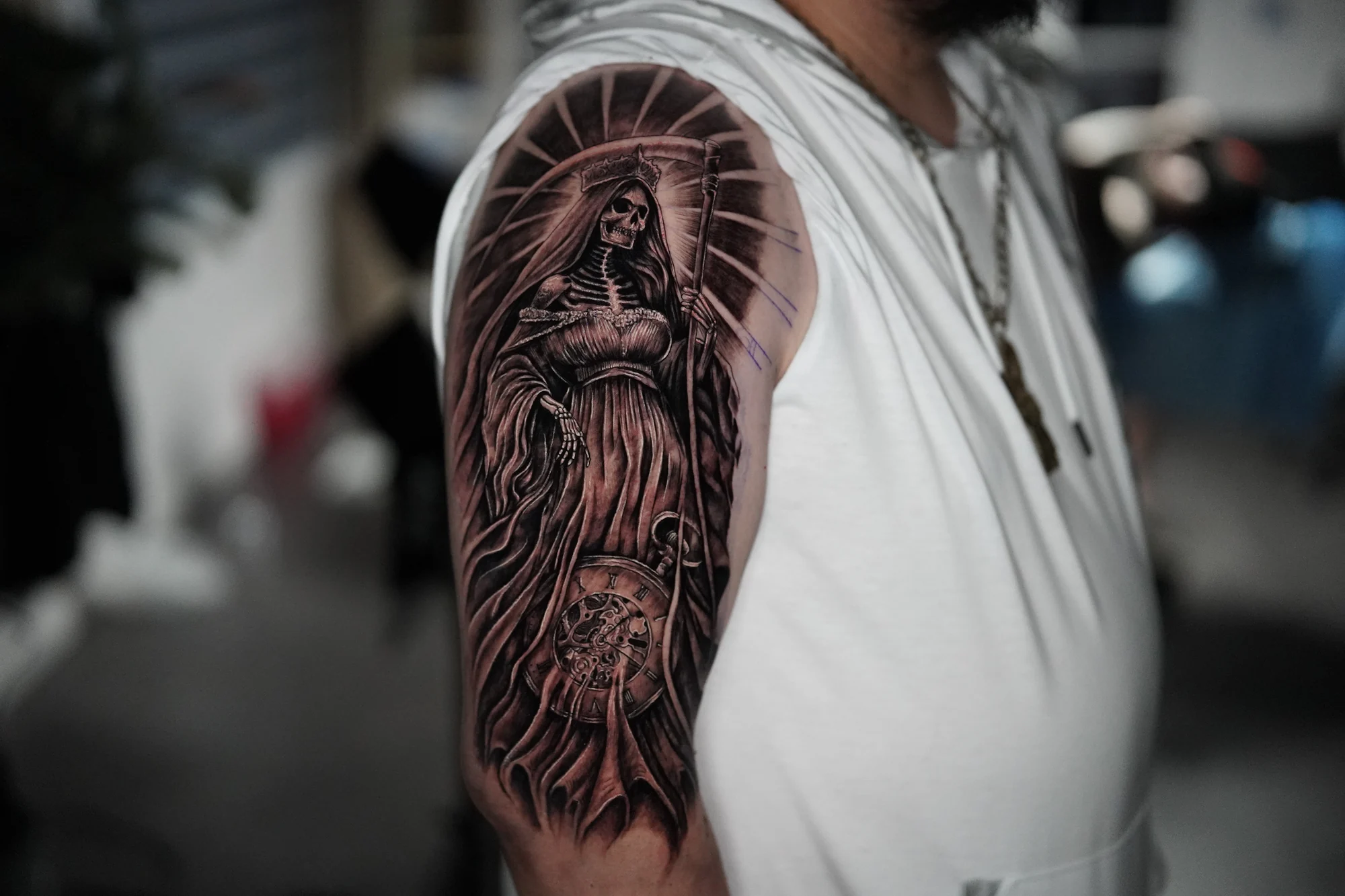 A robed female religious figure with a radiant halo and a clock face in a black-and-gray upper-arm tattoo.