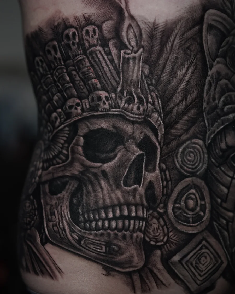 Alternate view. A large black-and-gray torso composition with a skull in a feathered headdress and a sculptural face framed by an animal headdress.