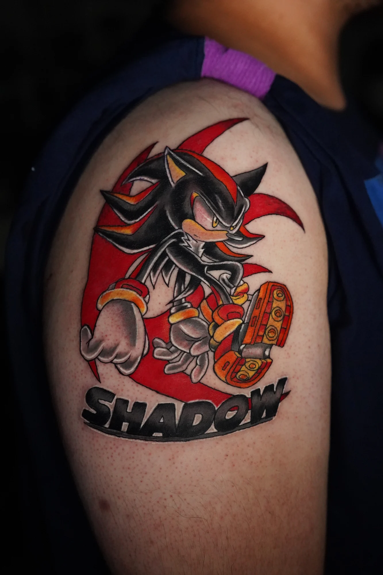 A red, black and yellow Shadow the Hedgehog tattoo with the character's name beneath the figure.