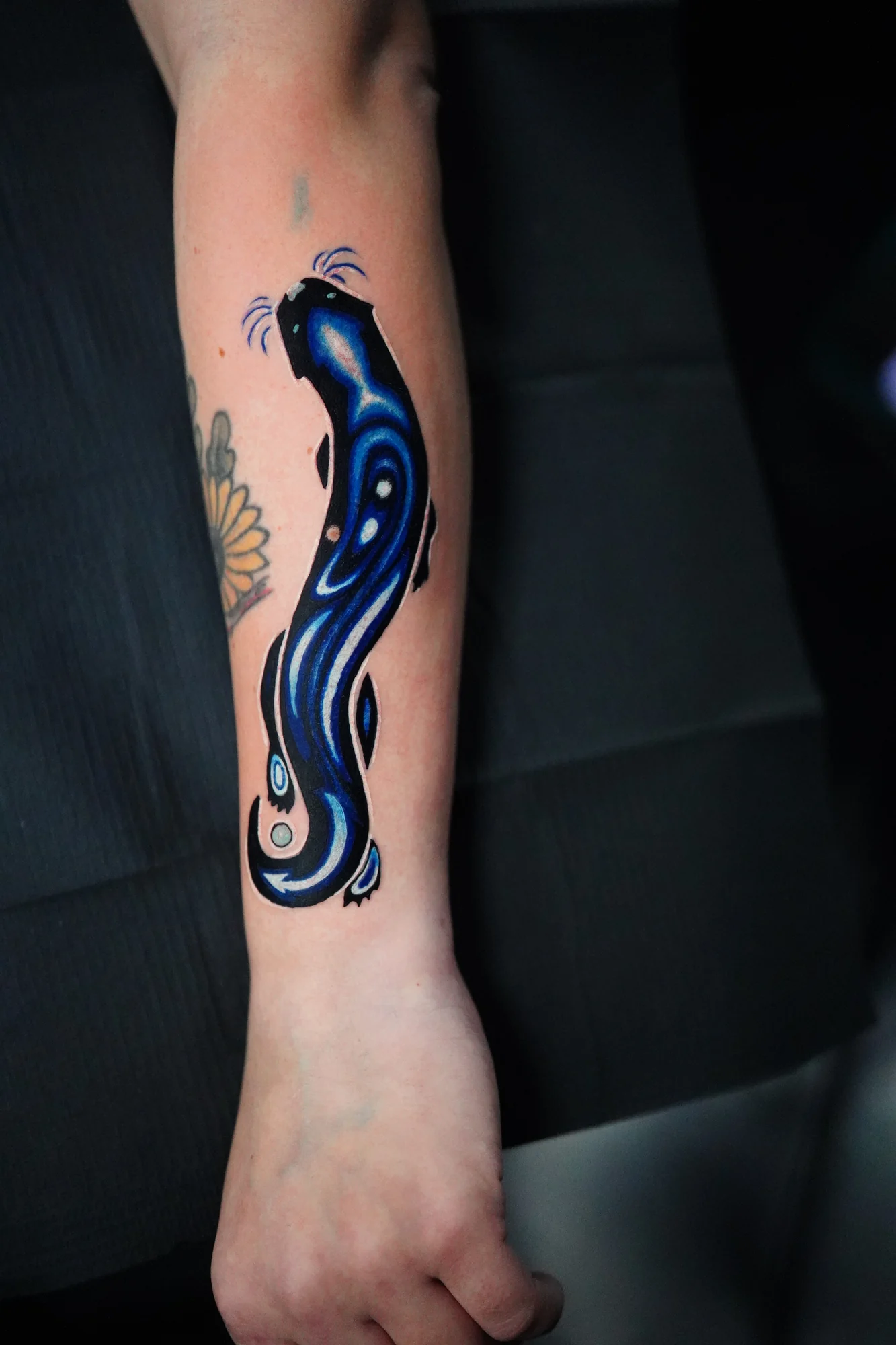 A flowing abstract blue and black tattoo with white highlights running down the forearm.