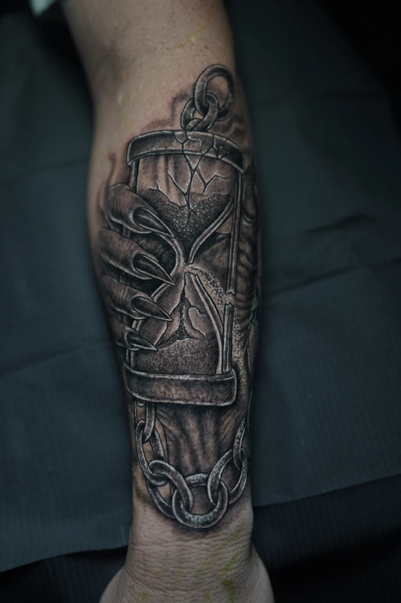 An ornate hourglass tattoo with curling supports and a dark winged shape inside the glass.