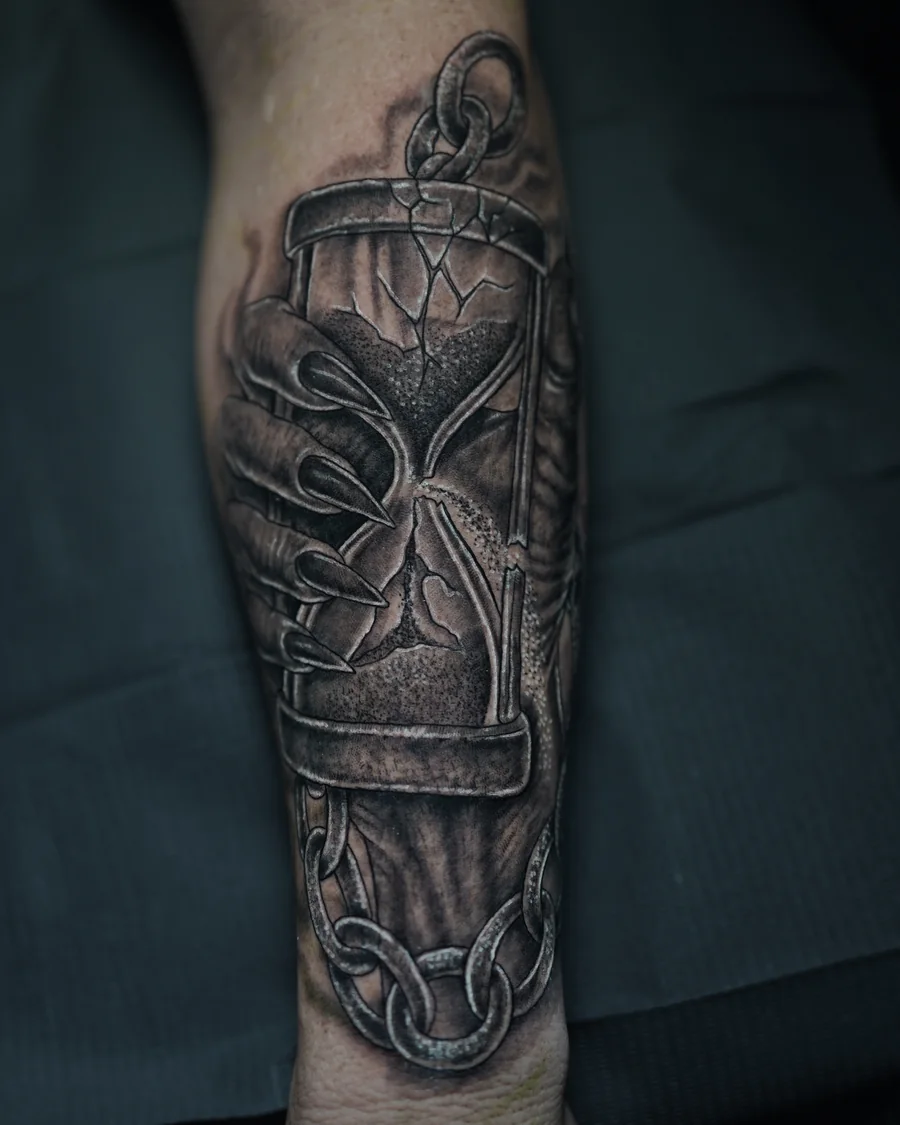 An ornate hourglass tattoo with curling supports and a dark winged shape inside the glass.