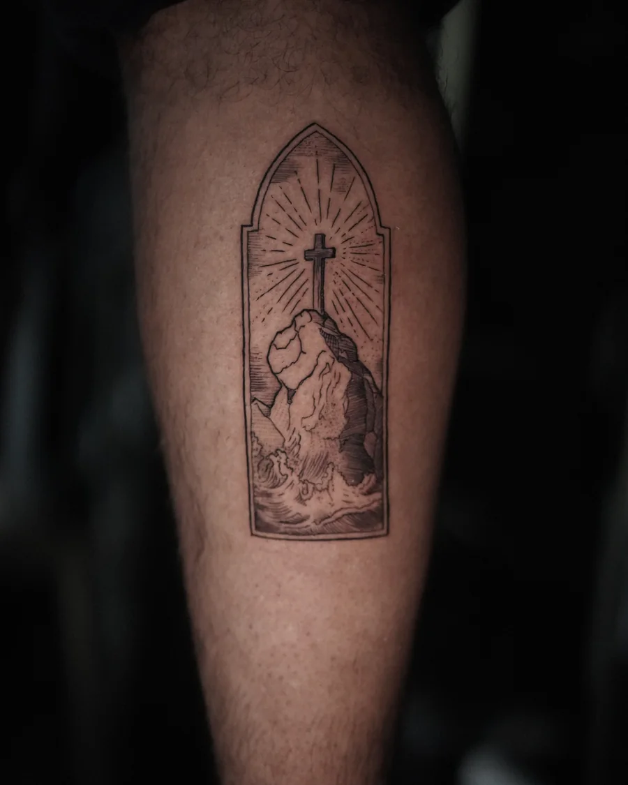 A pointed window-shaped tattoo enclosing clasped hands, a cross and rays of light in fine black linework.