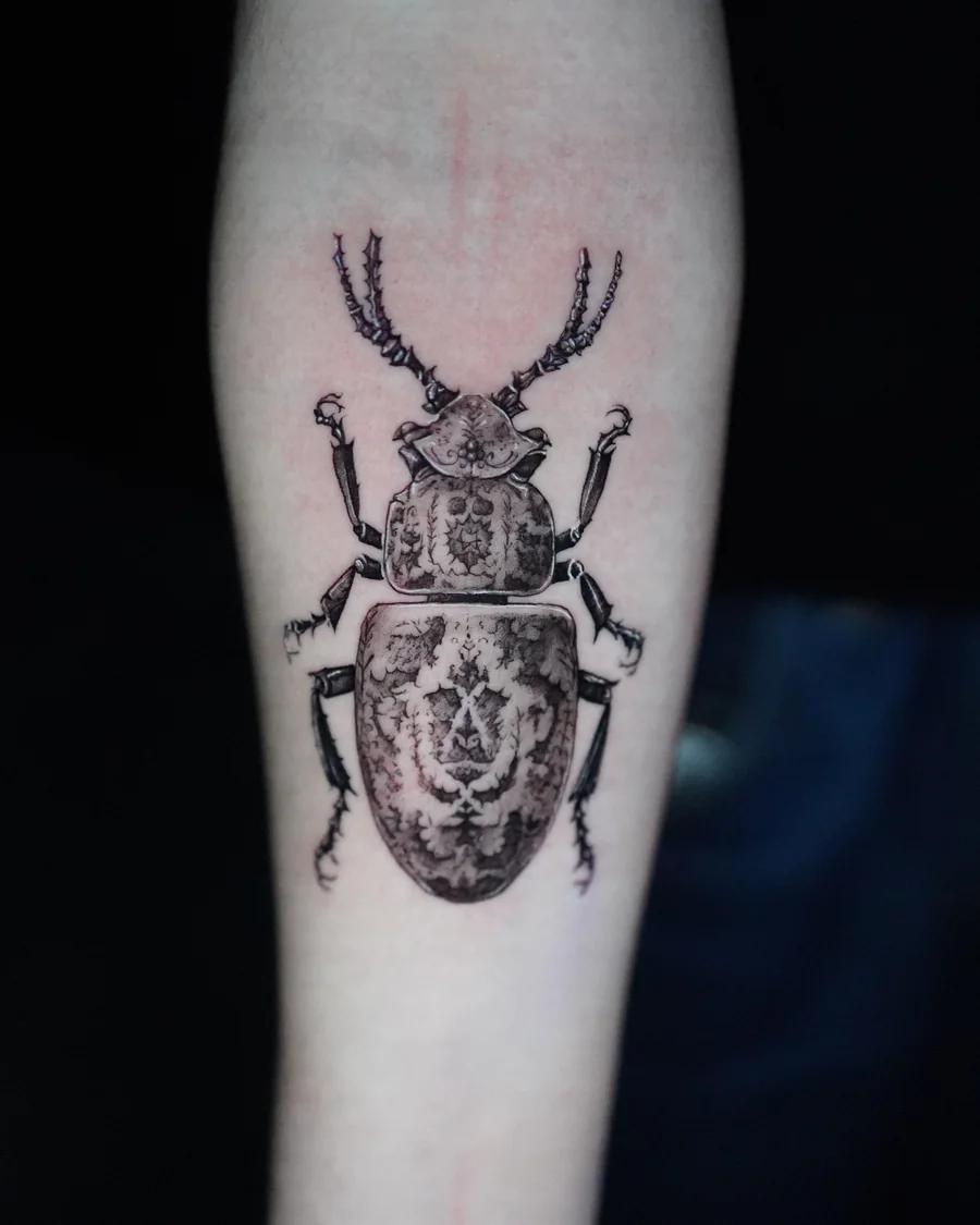 A stag beetle tattoo with branching mandibles and an ornamental pattern across its shell.
