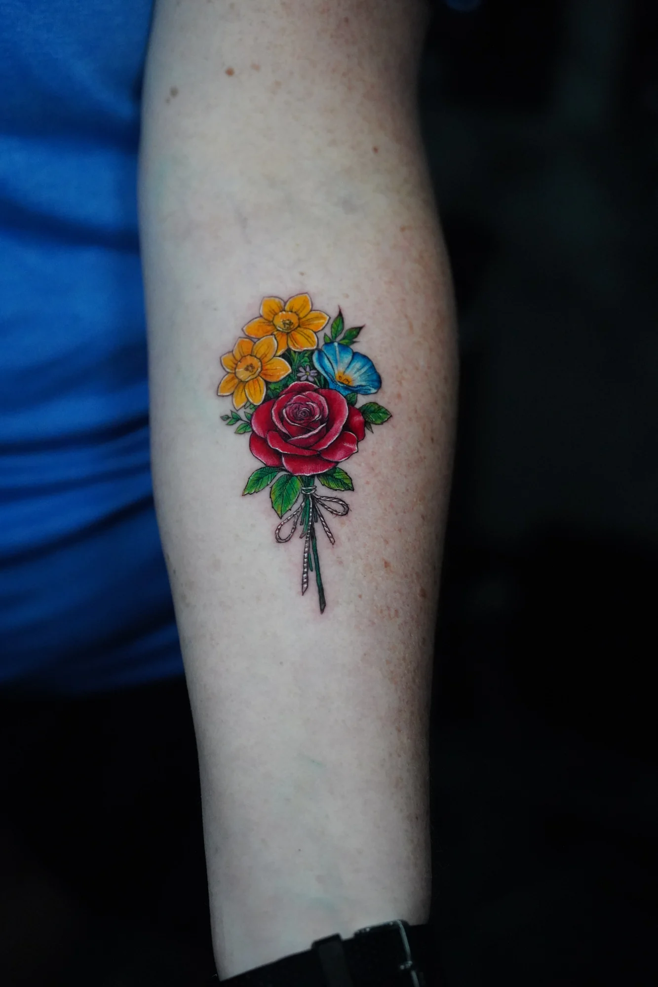 A small colorful bouquet of yellow, red and blue flowers with slender stems on the forearm.