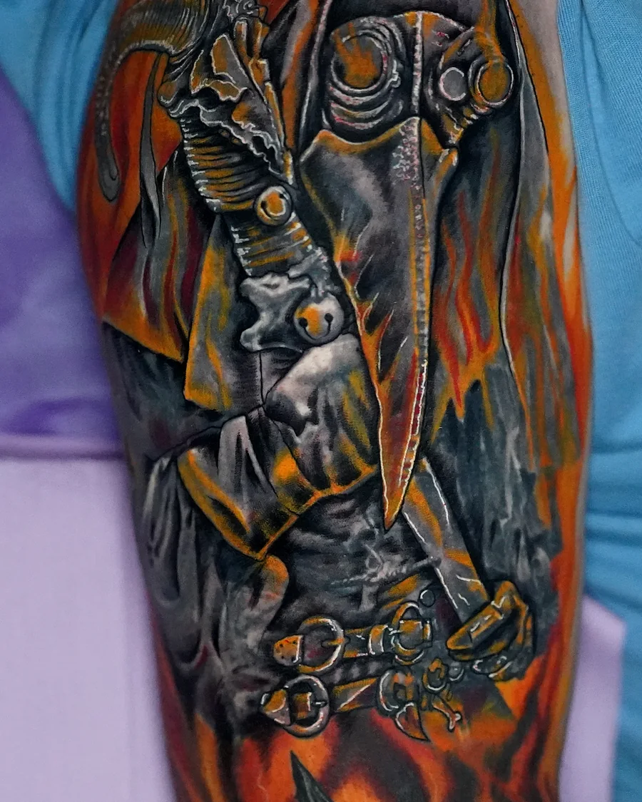 A winged skeletal figure wearing a gas mask, surrounded by orange flames in a color upper-arm tattoo.