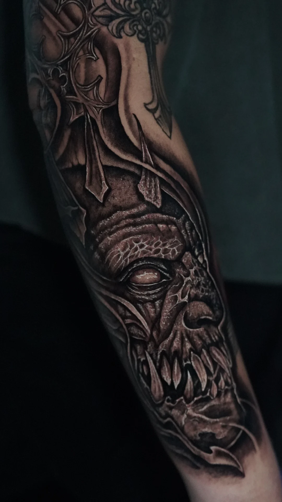 An elongated skull face with dark eye sockets and flowing textured shapes in a black-and-gray arm tattoo.
