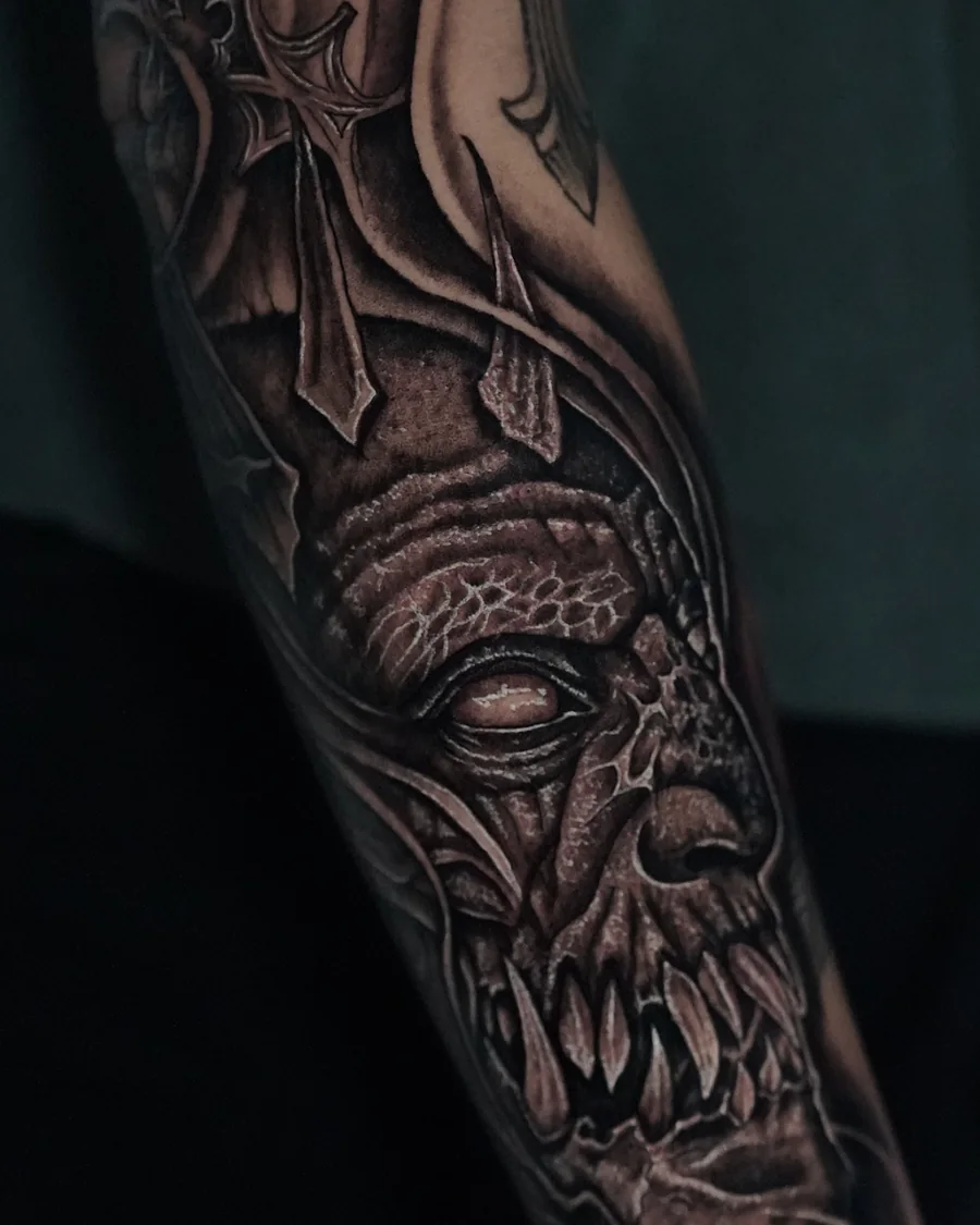 An elongated skull face with dark eye sockets and flowing textured shapes in a black-and-gray arm tattoo.