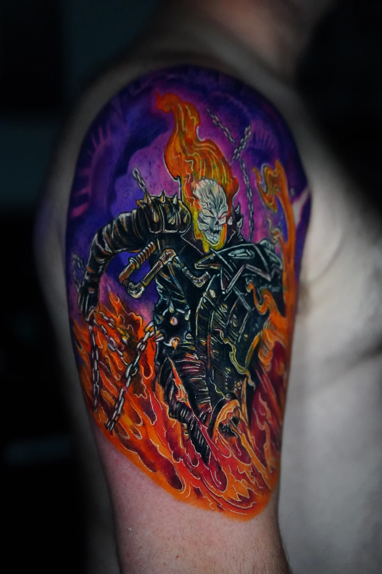 A flaming skull rider in a dark jacket with a chain, surrounded by vivid orange fire and a purple background.