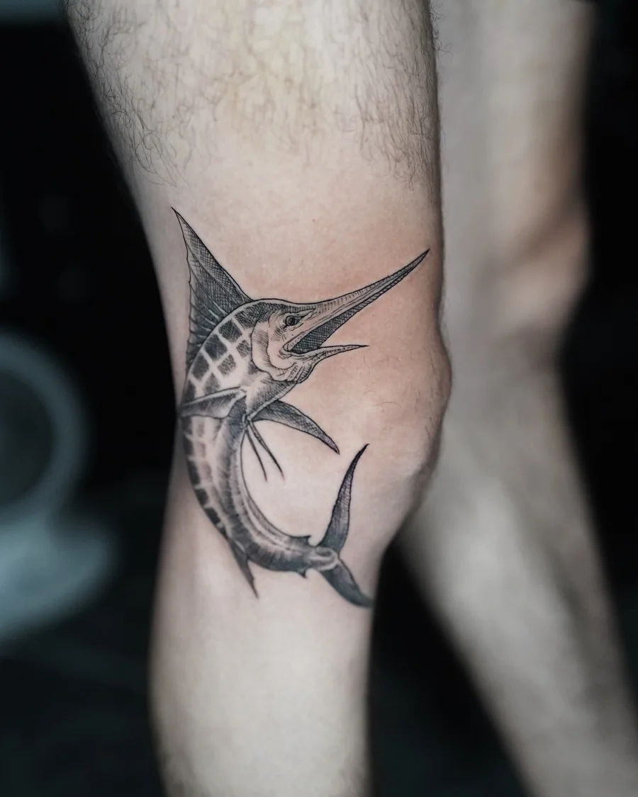 Alternate view. A curved marlin tattoo with a long pointed bill and a patterned back, rendered in black and gray on the arm.